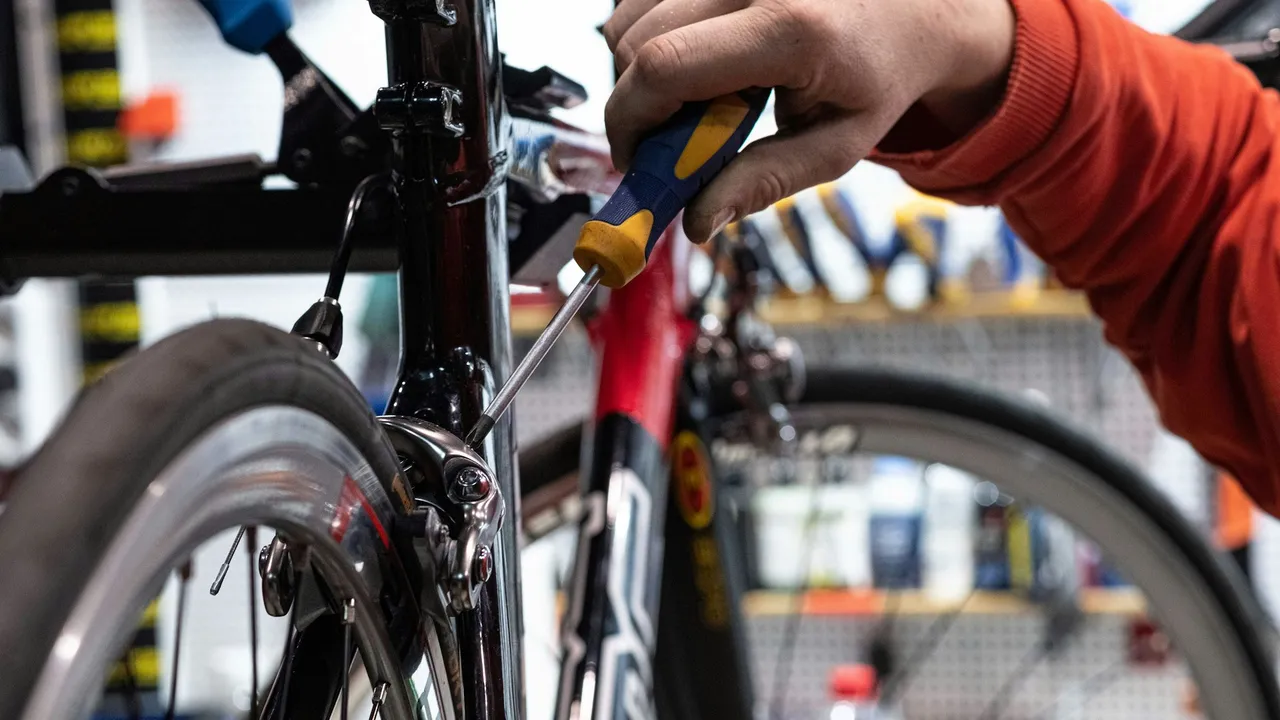 A mechanic working on a bicycle held in a repair stand, the front wheel and fork in frame.