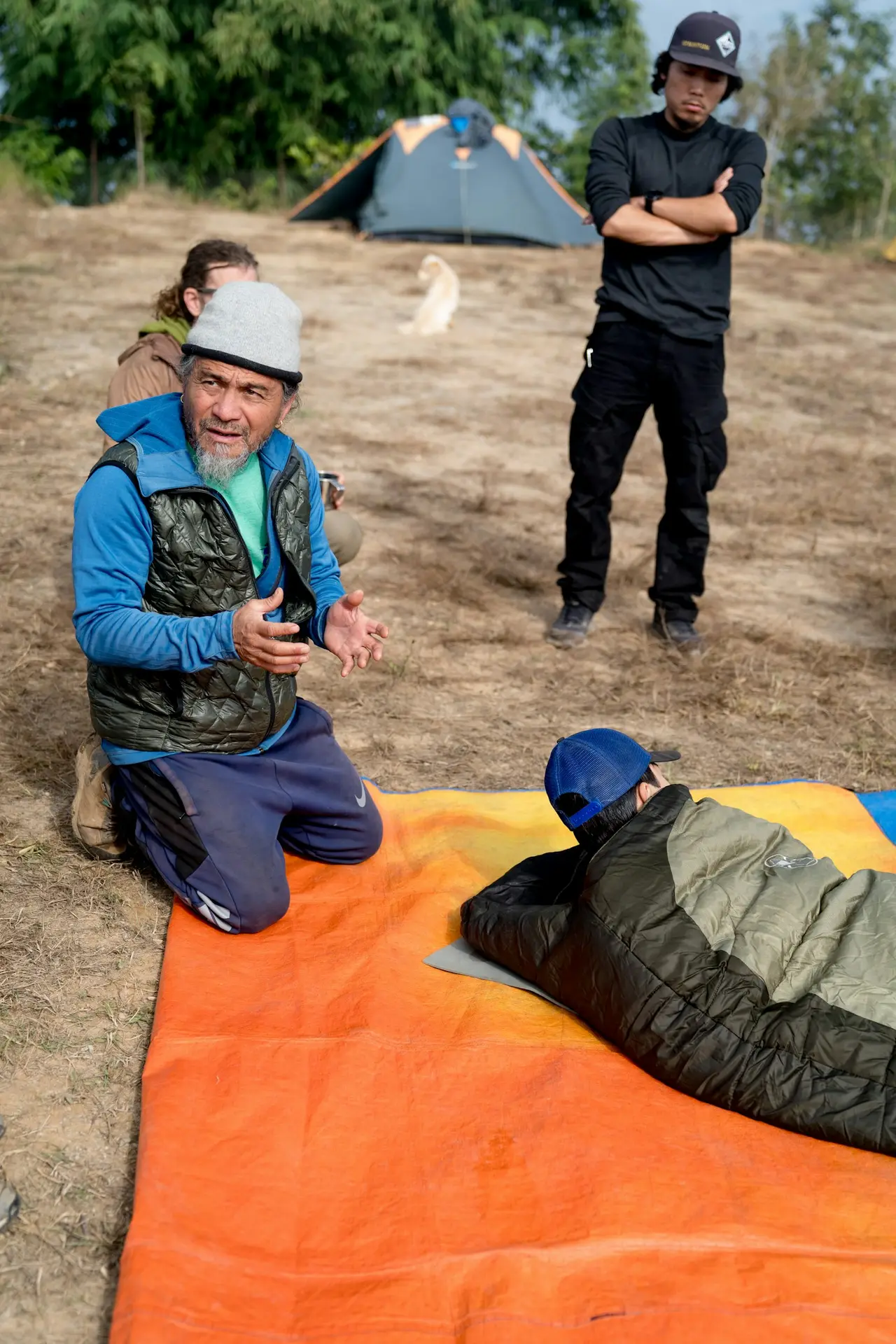Two people at a camp beside tents with gear spread out.