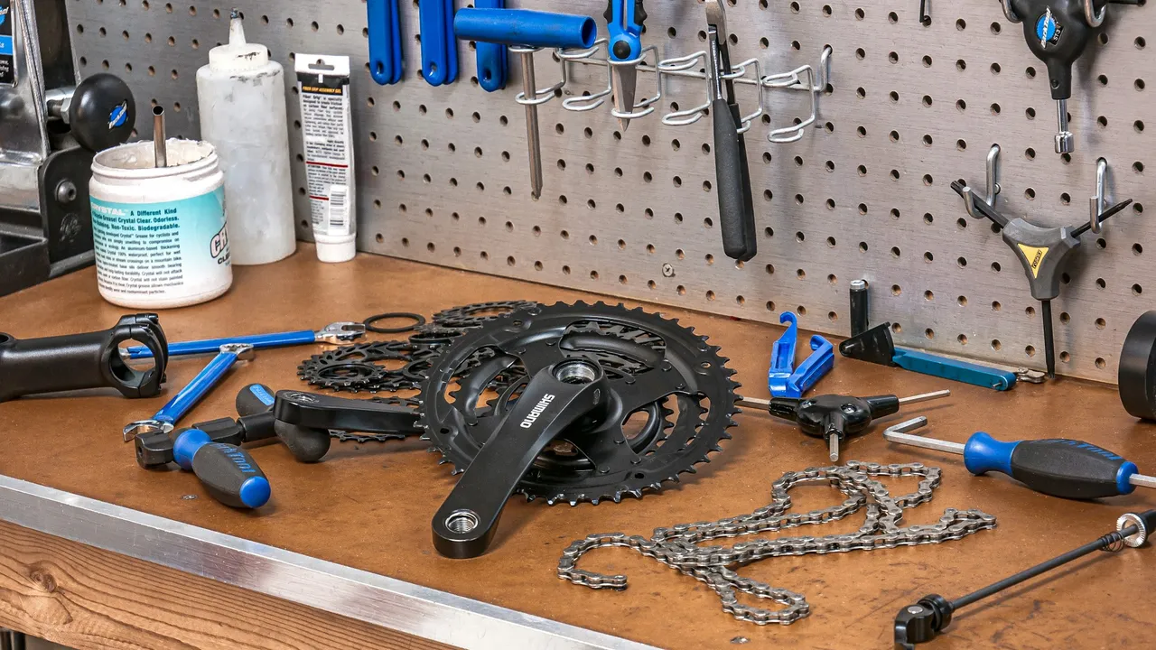 A workbench with a chainset, two chains and a spread of bike tools laid out in front of a pegboard.