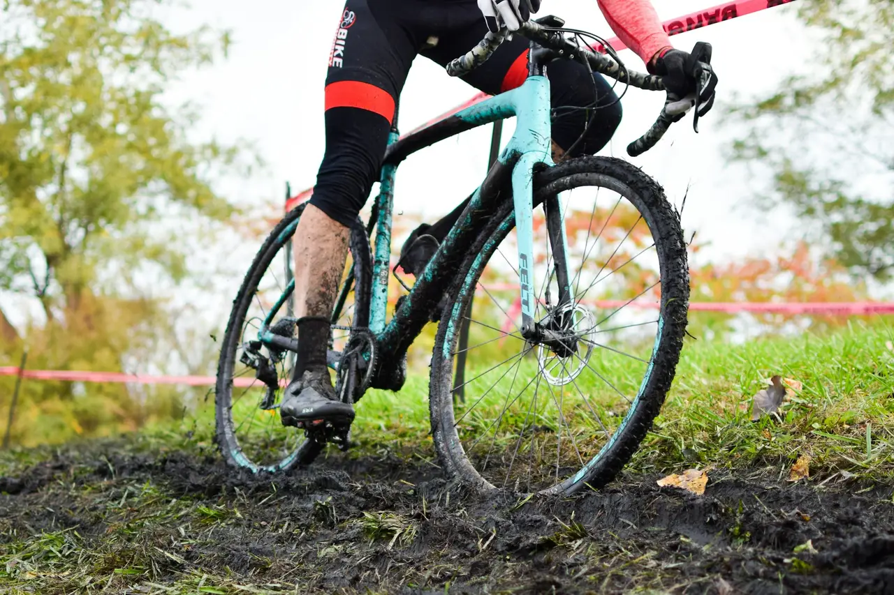 A cyclocross rider riding through deep mud, drivetrain and legs spattered.