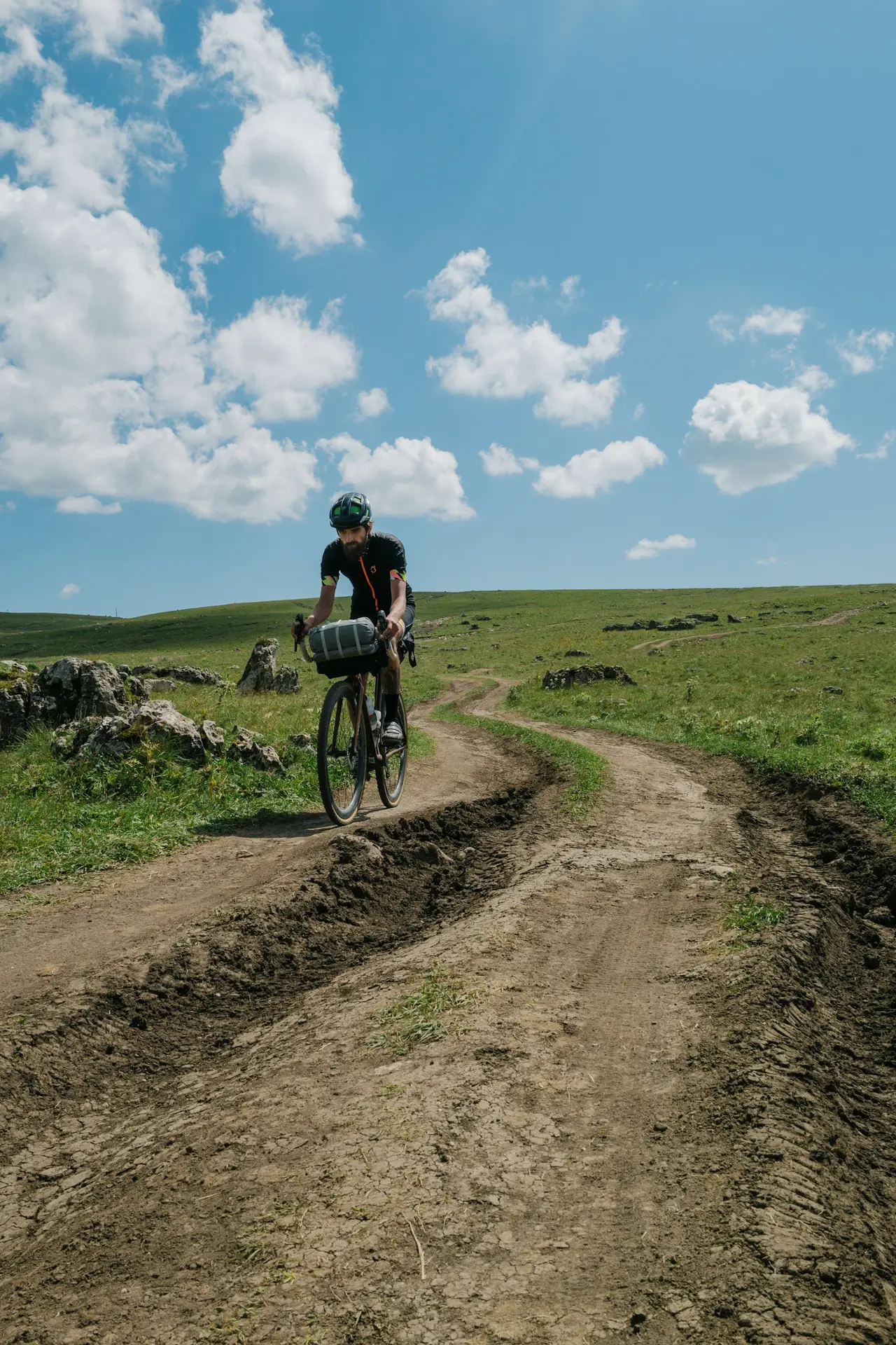 Two riders on loaded bikes climbing a dirt road under a wide sky.