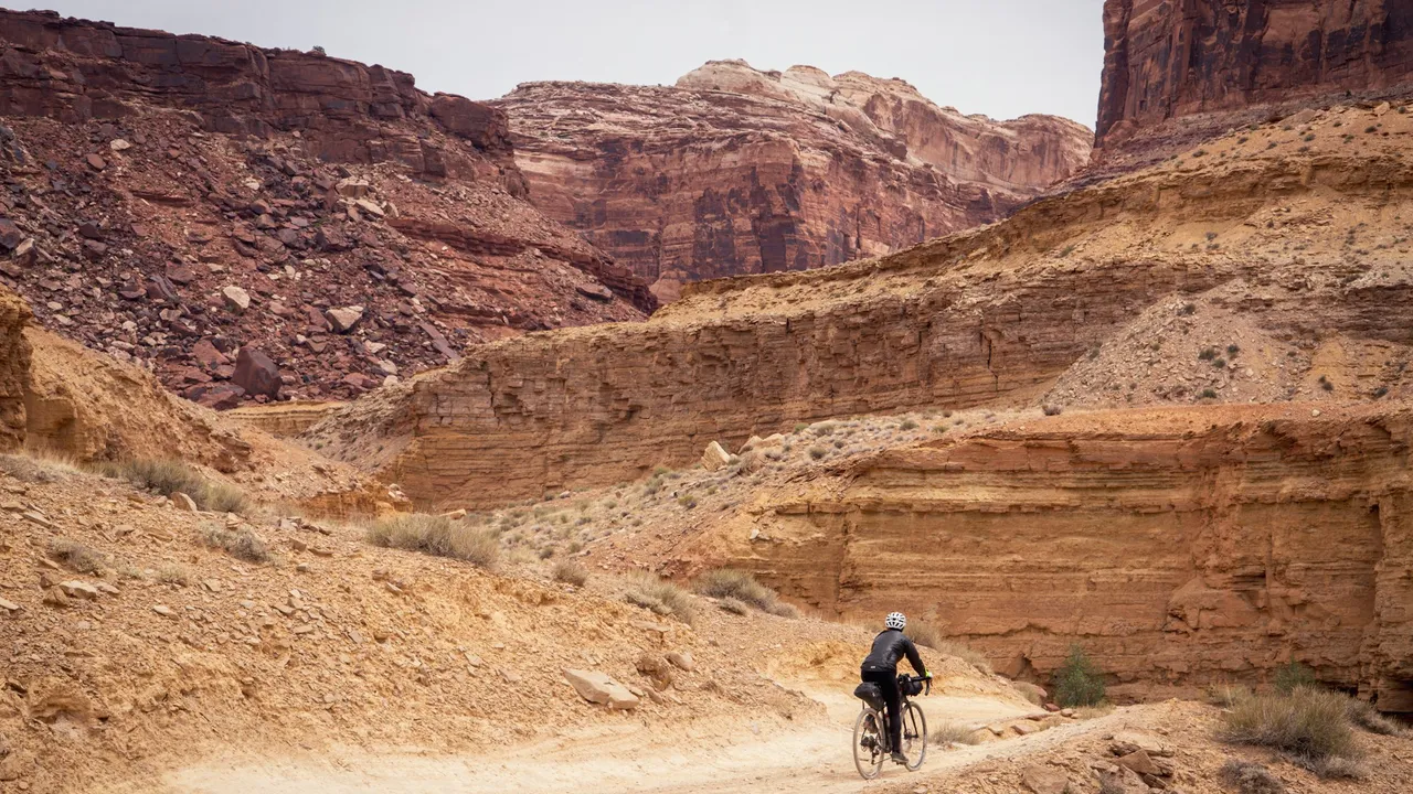 A lone rider on a dirt road far below layered red canyon walls.