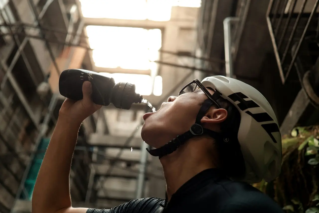 A rider tipping a bottle back to drink while stopped in an alley.
