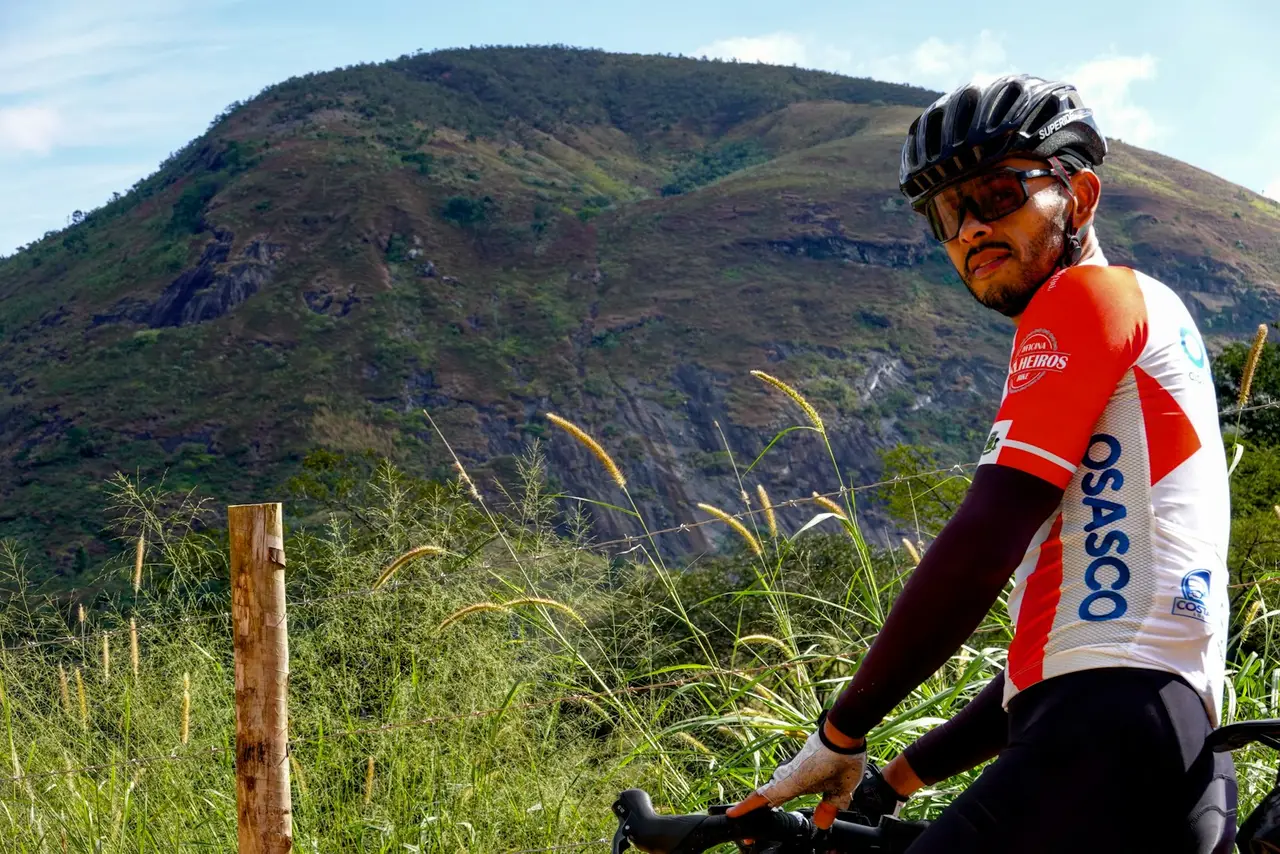 A cyclist standing beside a bike with hills behind, the frame's main triangle in view.