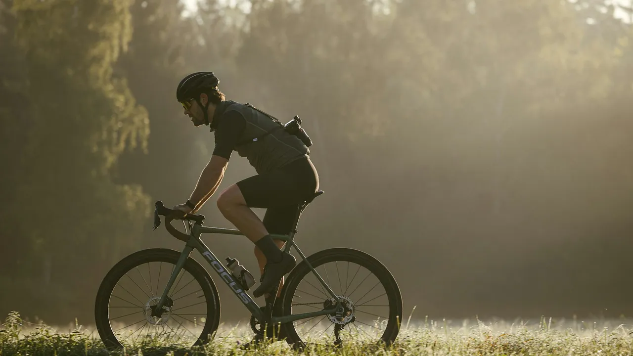 A rider on a gravel bike crossing a misty field in low morning sun.