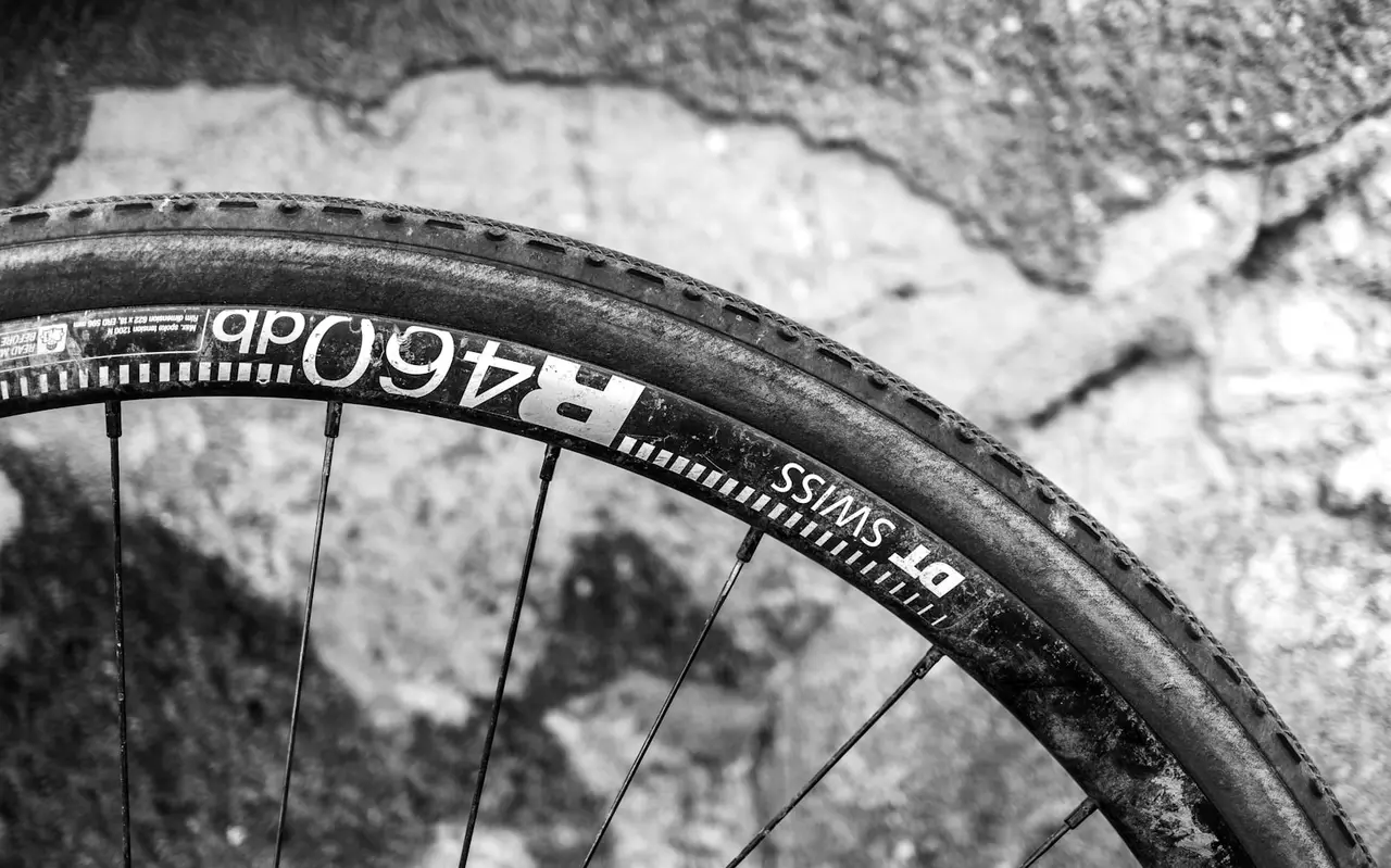 Black and white close-up of a gravel tyre and rim resting on rock, tread blocks along the crown and the thinner sidewall curving away underneath.