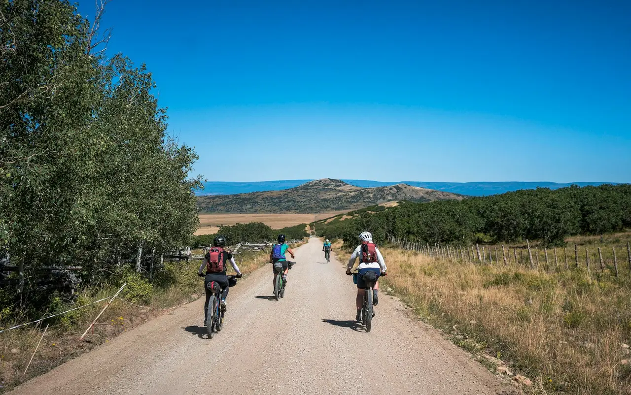 A group of riders on loaded bikes on a gravel road between fields.