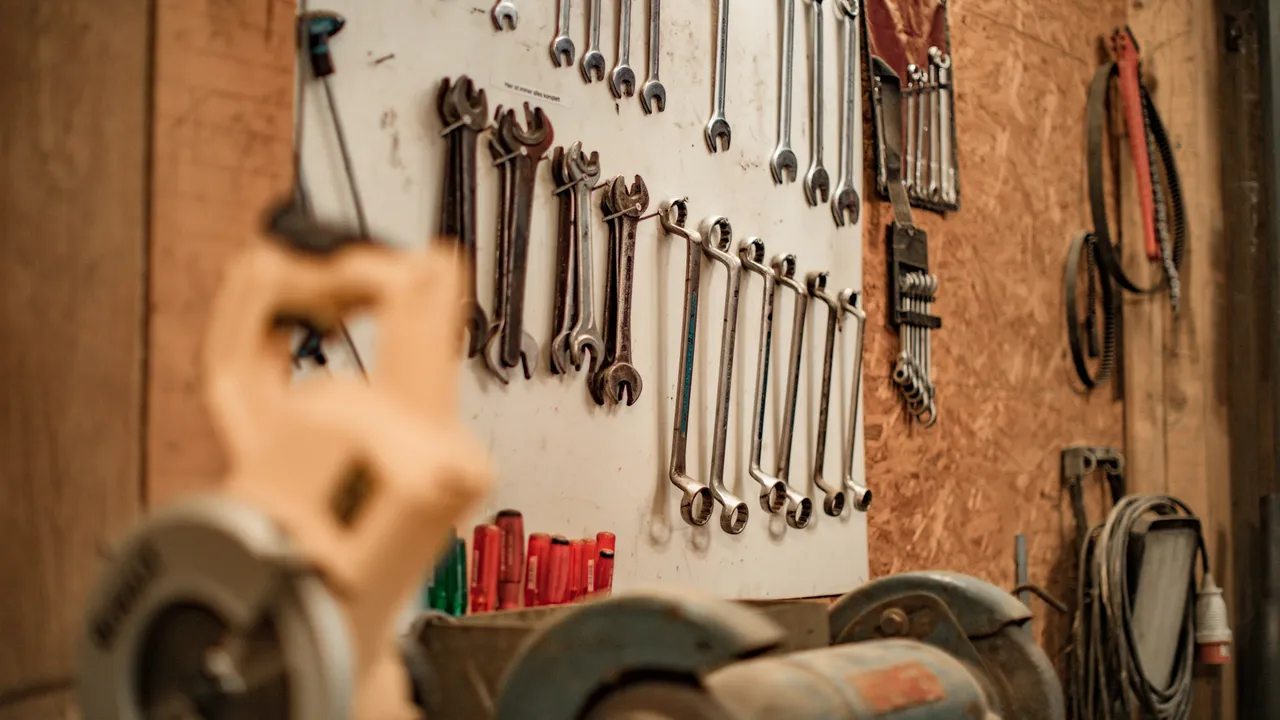 A workshop wall hung with spanners and hand tools, a vice in the foreground.
