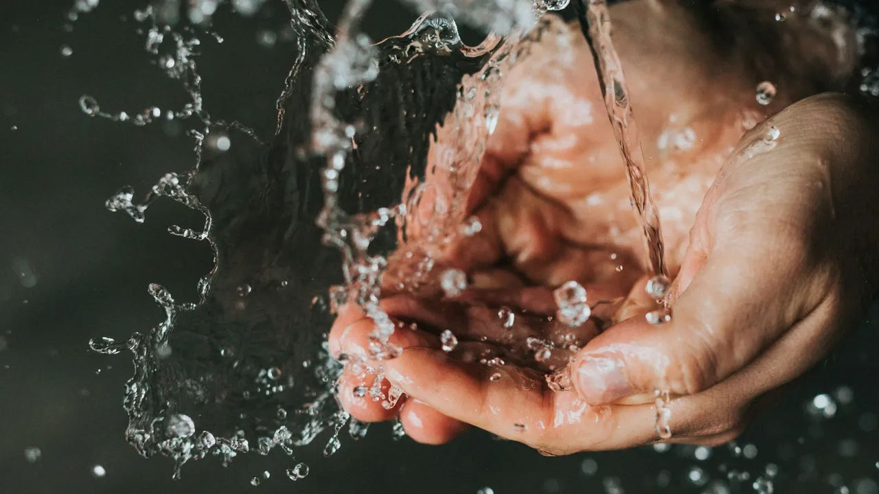Cupped hands catching a stream of running water against a dark background.
