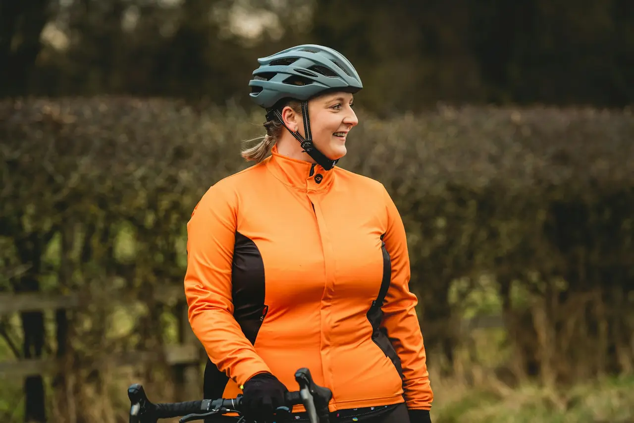 A rider in an orange jacket and helmet on a bike in cold, damp conditions.