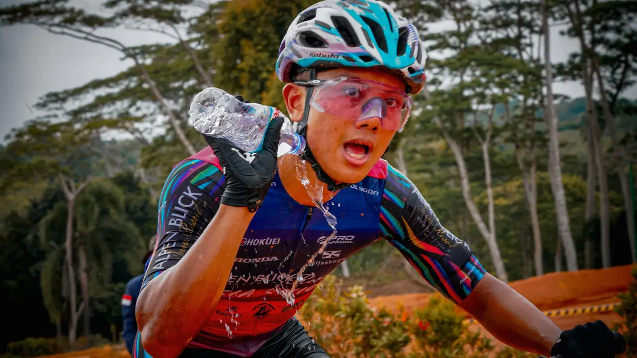 A cyclist pouring water over their head to cool off.