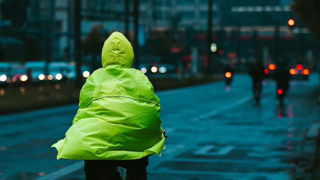 A cyclist in a bright green rain cape riding a flooded street at dusk.
