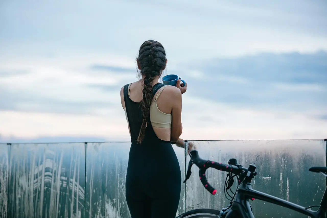 A rider standing with their bike, seen from behind, looking out over a landscape.