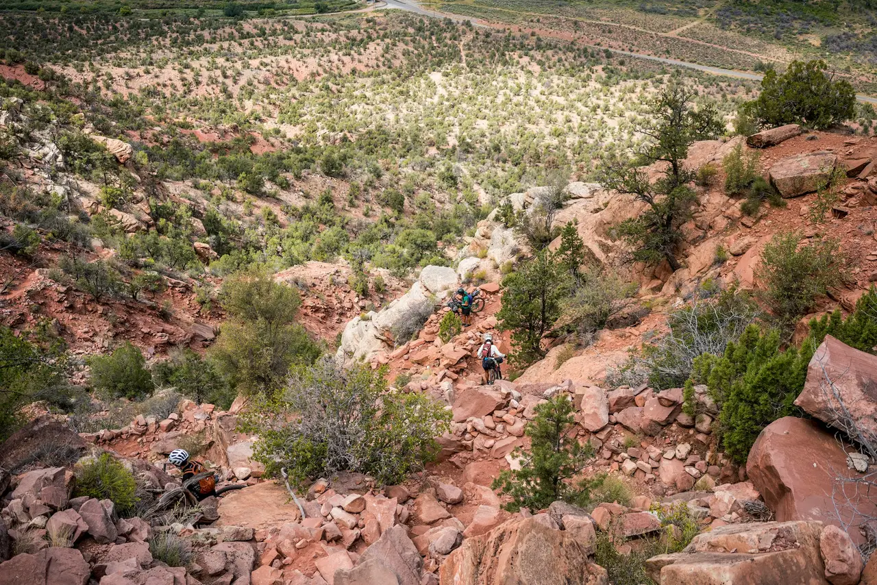 Two riders on a dirt road winding through red rock country.