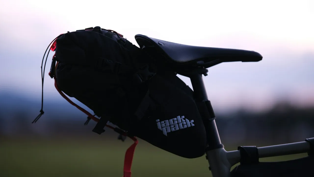 A large black seat pack strapped under a saddle, seen in profile against a pale evening sky.