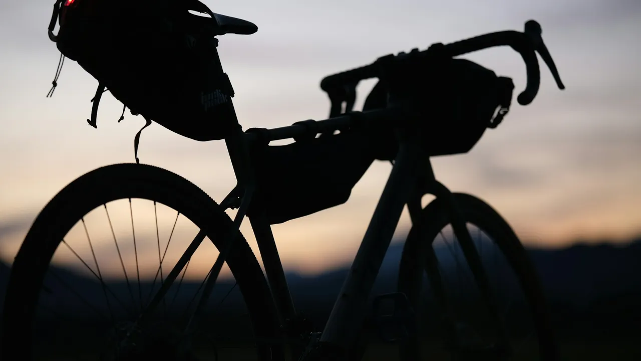 The silhouette of a bike carrying a seat pack and a bar bag against a dusk sky.