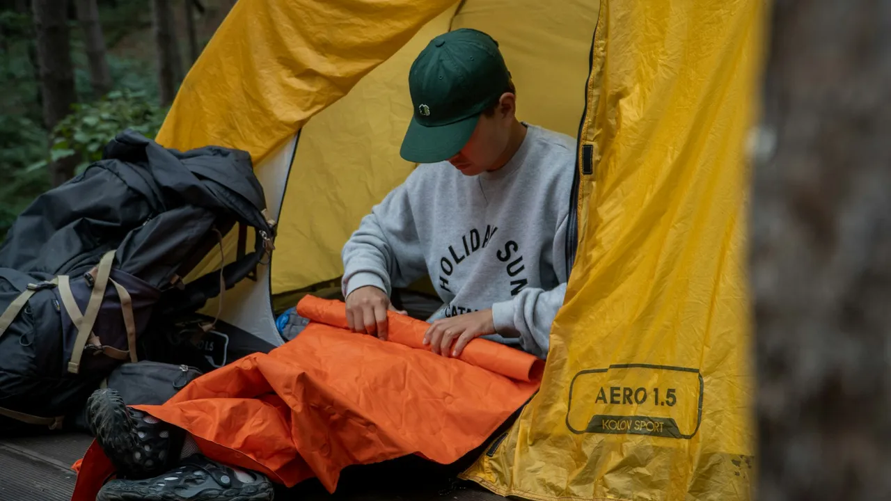 A rider unrolling an orange inflatable sleeping pad in a tent doorway, packs stacked beside them.