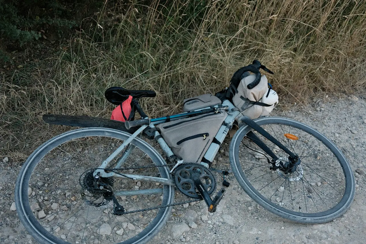 A loaded touring bike lying on its side on a gravel path, seat pack and rear wheel in view.