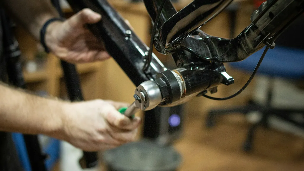Close-up of hands using a tool on a bicycle held in a workshop stand.